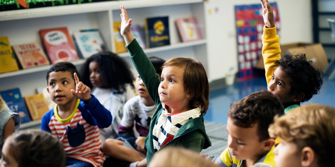 Young children sitting in a classroom raising their hands, learning social and emotional skills